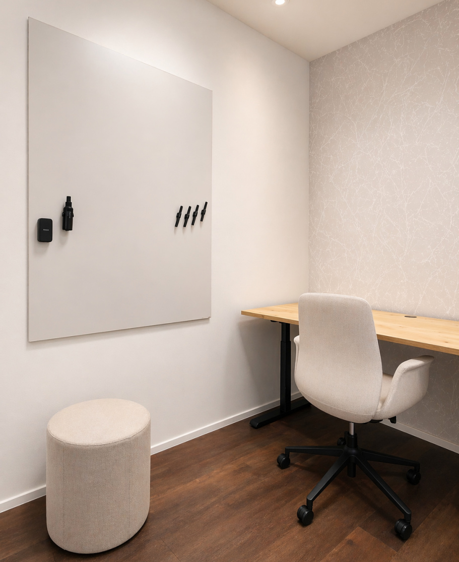 Loungebereich mit taupefarbenen Sofas und senffarbenen Kissen um einen Couchtisch, an der Wand ein Bildschirm mit Kamera vor Holzlamellen